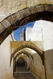 Image du Maroc Professionnelle de  Dans une rue des Habous, la succession des balèvres, moulure, arches, portiques et autres éléments décoratifs, projetent les visiteurs dans l’ardeur avec un élan de force et de fierté d’une époque révolue. Conçu par les architectes Auguste Cadet et Edmond Brion d’après l’ébauche d’un premier plan-masse dû à Albert Laprade, le quartier fait partie des endroits les plus pittoresques de Casablanca, il fut La construction n’avait commencé qu’après la première guerre mondiale. Situé près du Palais Royale, ce joyau architectural fait partie du patrimoine architectural de la ville, Samedi 8 Novembre 2008. Au centre le minaret de La mosquée Ben Youssef. (Photo / Abdeljalil Bounhar)
